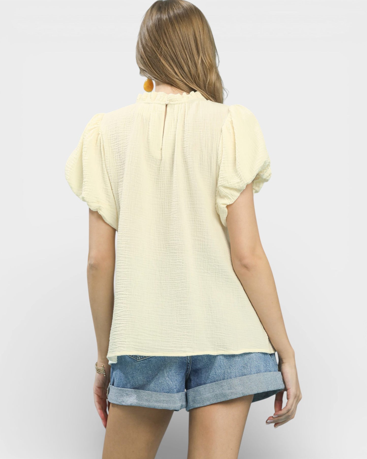 Woman wearing a light yellow top and denim shorts on a plain background