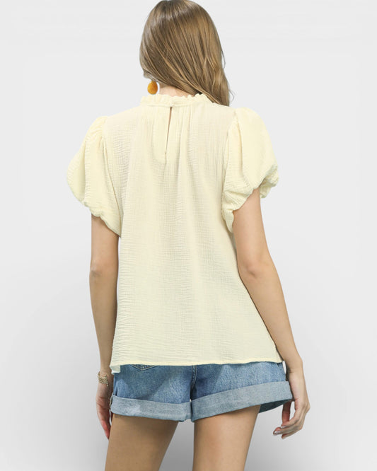 Woman wearing a light yellow top and denim shorts on a plain background