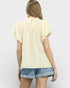 Woman wearing a light yellow top and denim shorts on a plain background
