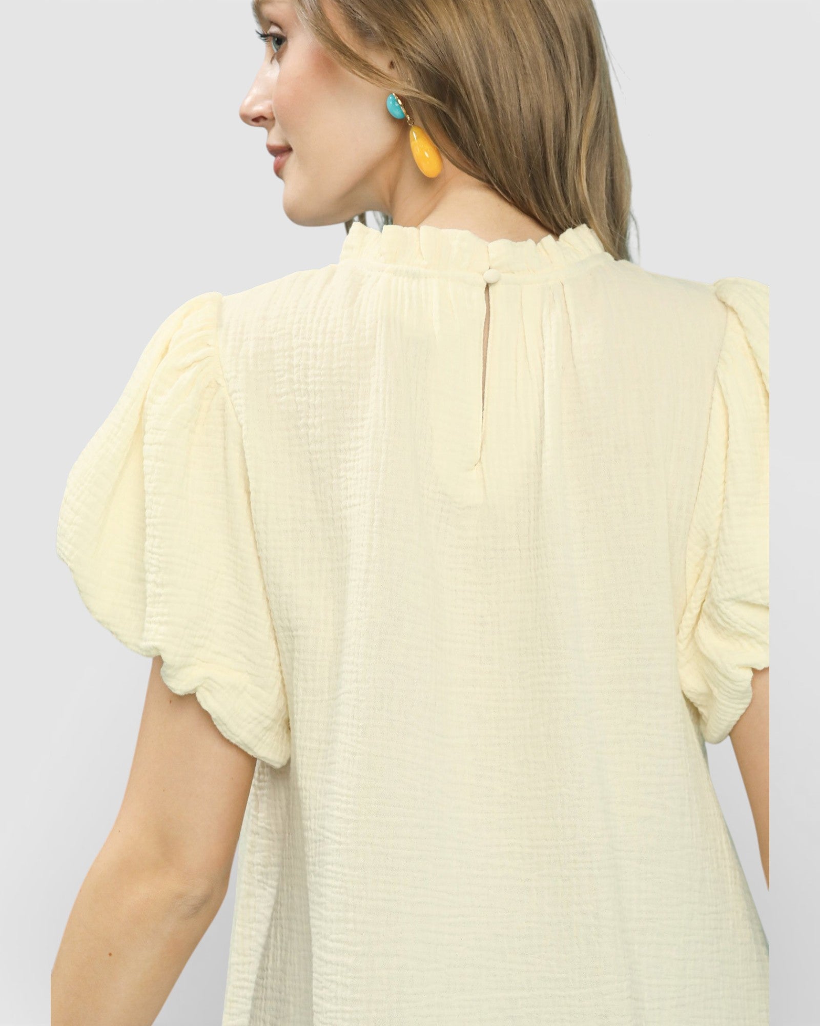 Woman wearing a light yellow blouse with short sleeves against a plain background