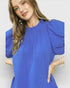 Woman wearing a blue dress with puffed sleeves against a plain background