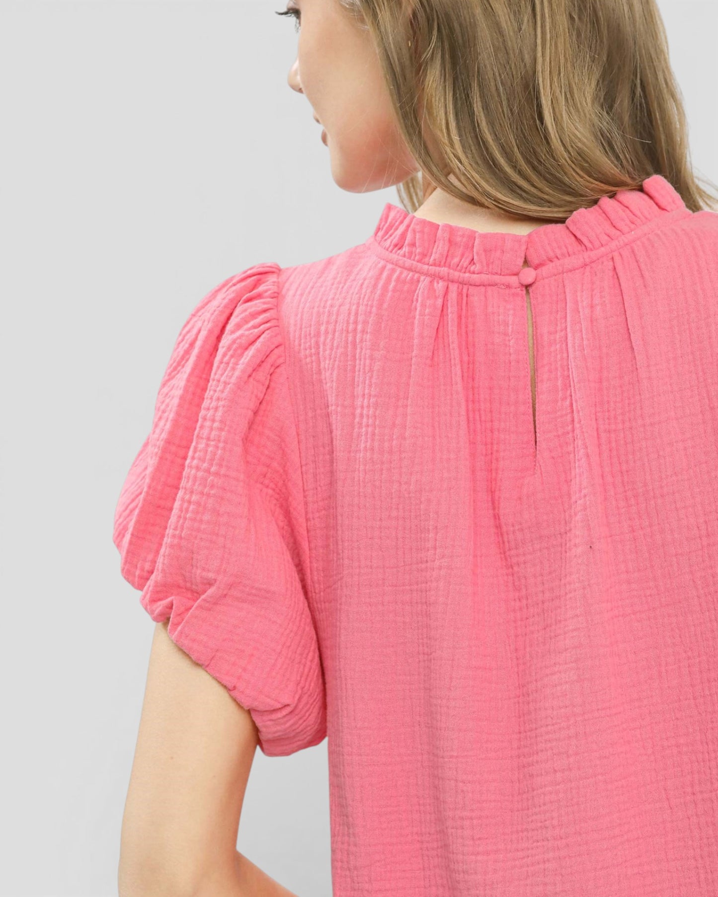 Close-up of a person wearing a pink textured top against a light gray background