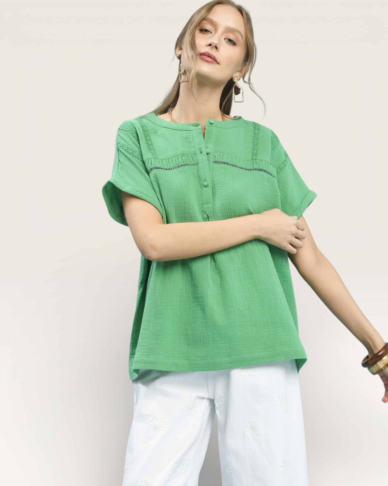 Woman wearing a green top and white pants on a plain background