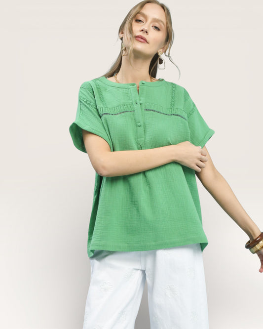 Woman wearing a green top and white pants on a plain background