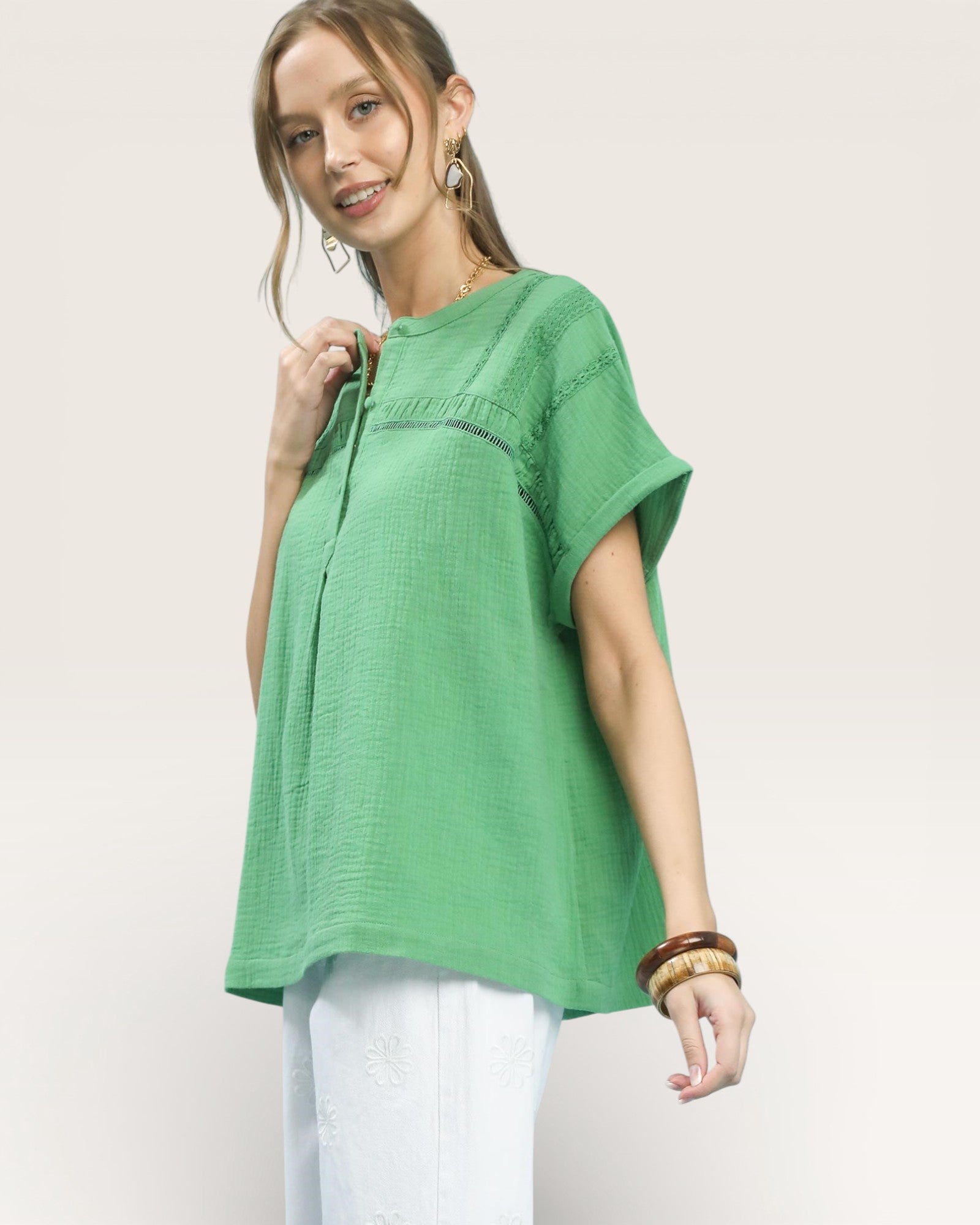 Woman wearing a green top and white pants on a plain background