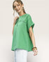 Woman wearing a green top and white pants on a plain background