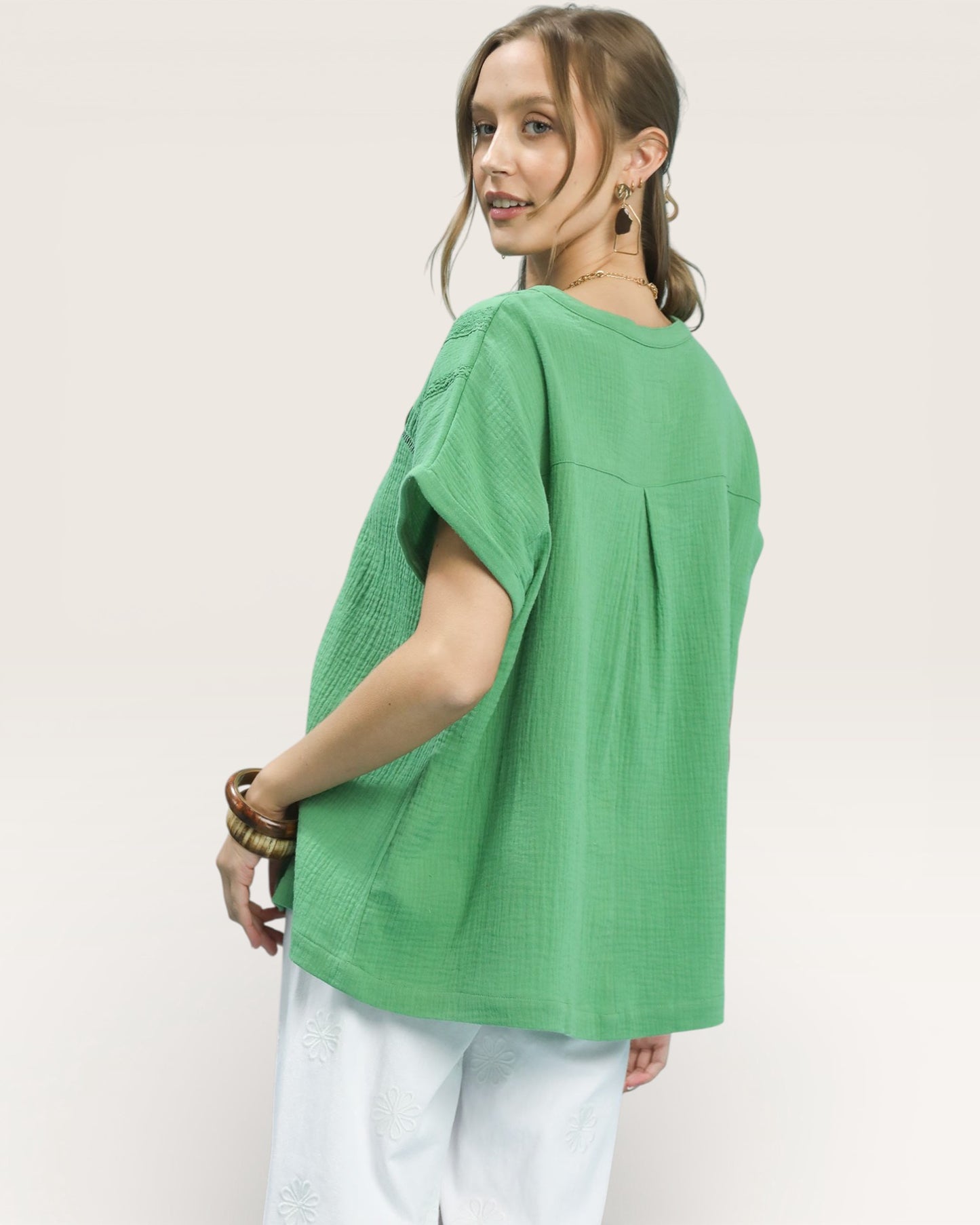 Woman wearing a green oversized shirt and white pants on a plain background