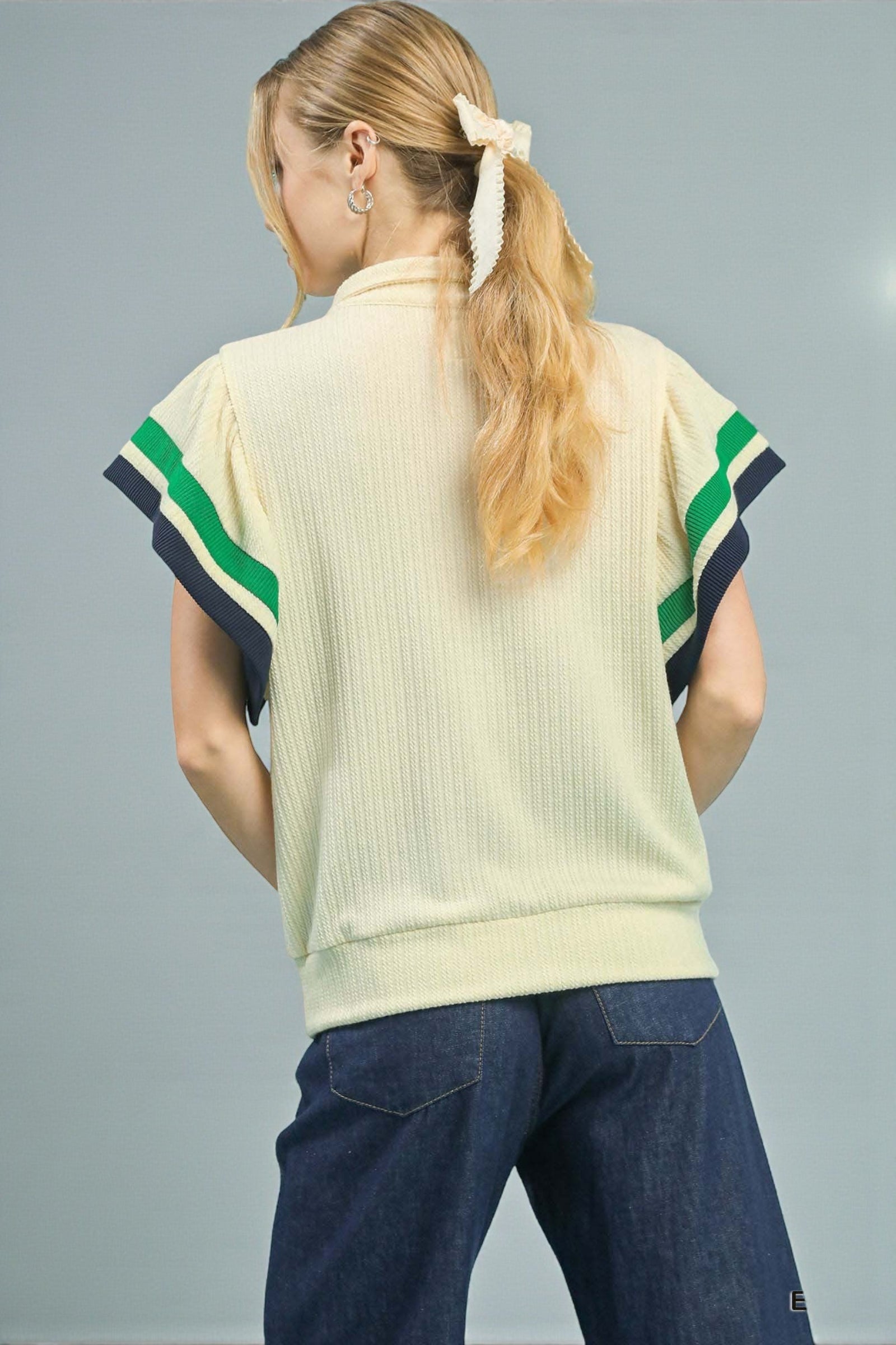 Person wearing a light-colored sweater with green and navy accents on a gray background