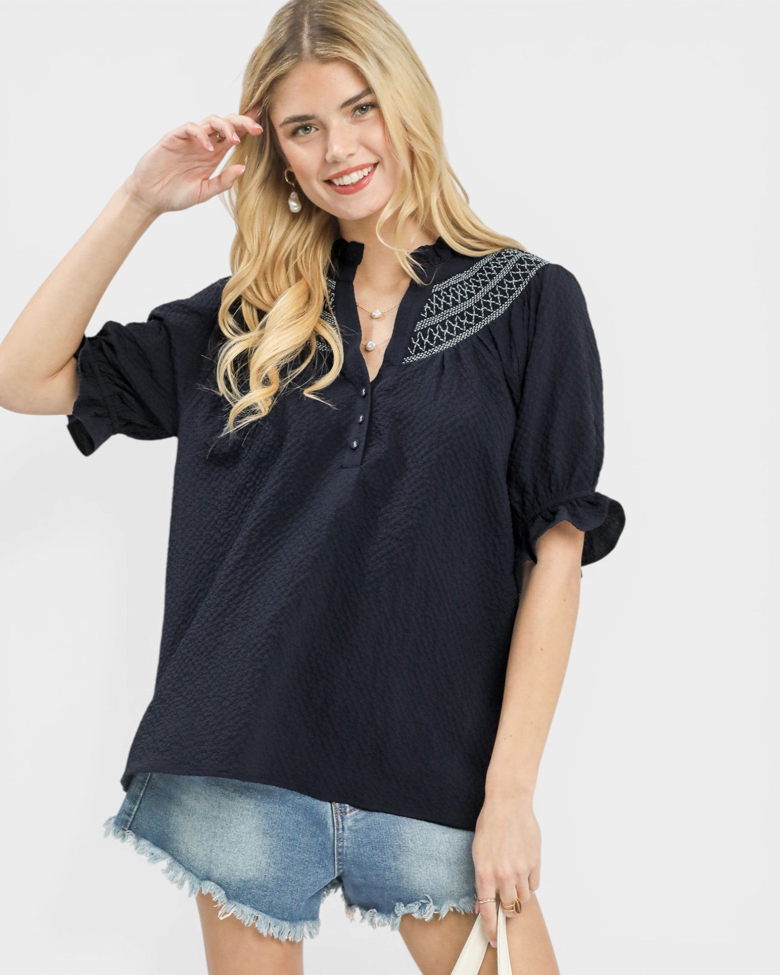 Woman wearing a black blouse with embroidery and denim shorts on a white background