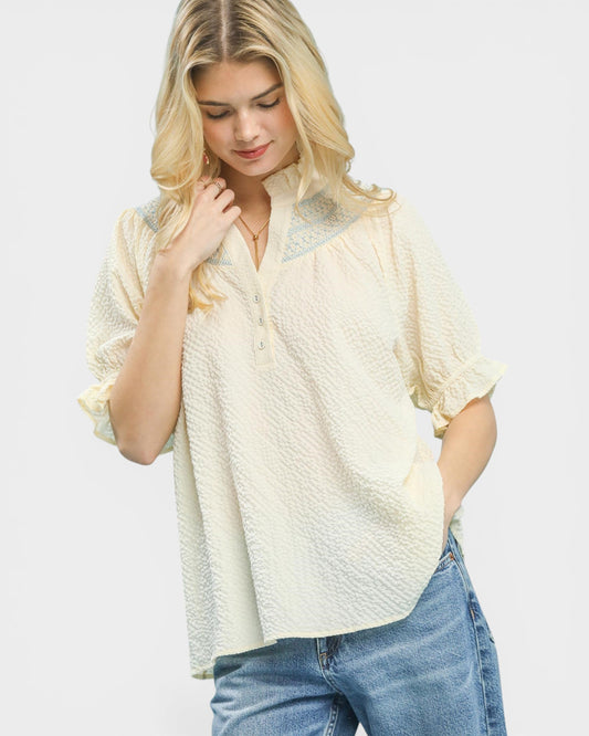 Woman wearing a light-colored blouse and blue jeans on a plain background