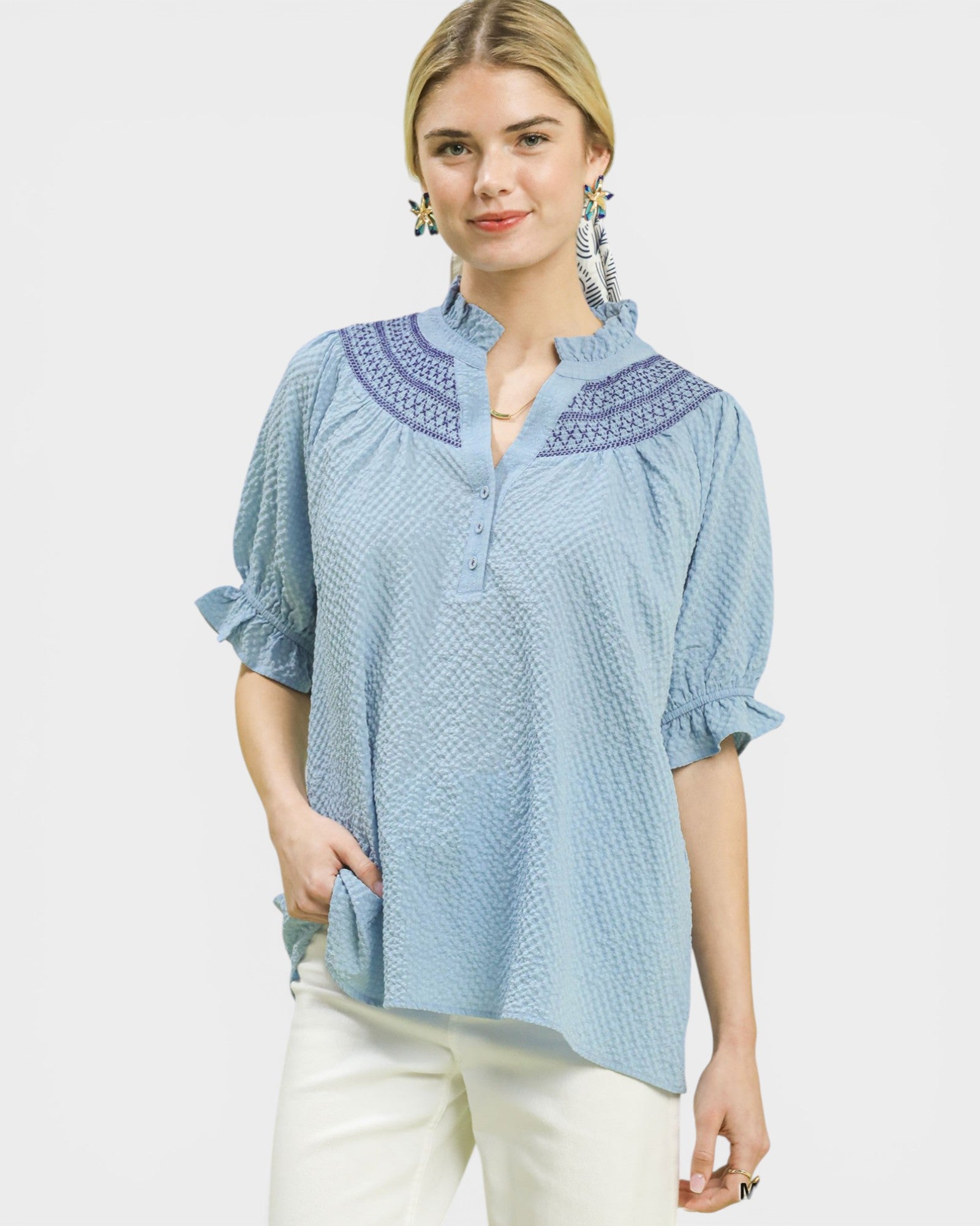 Woman wearing a light blue blouse with embroidered details on a white background