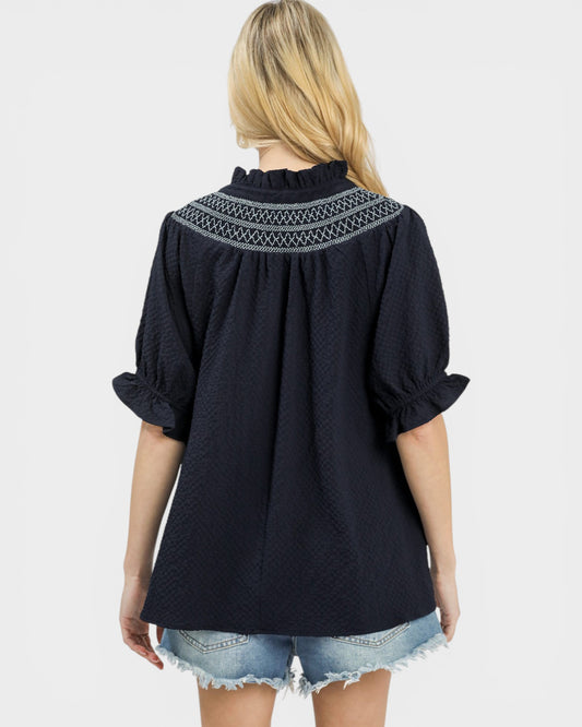 Black blouse with embroidered neckline worn by a person on a white background