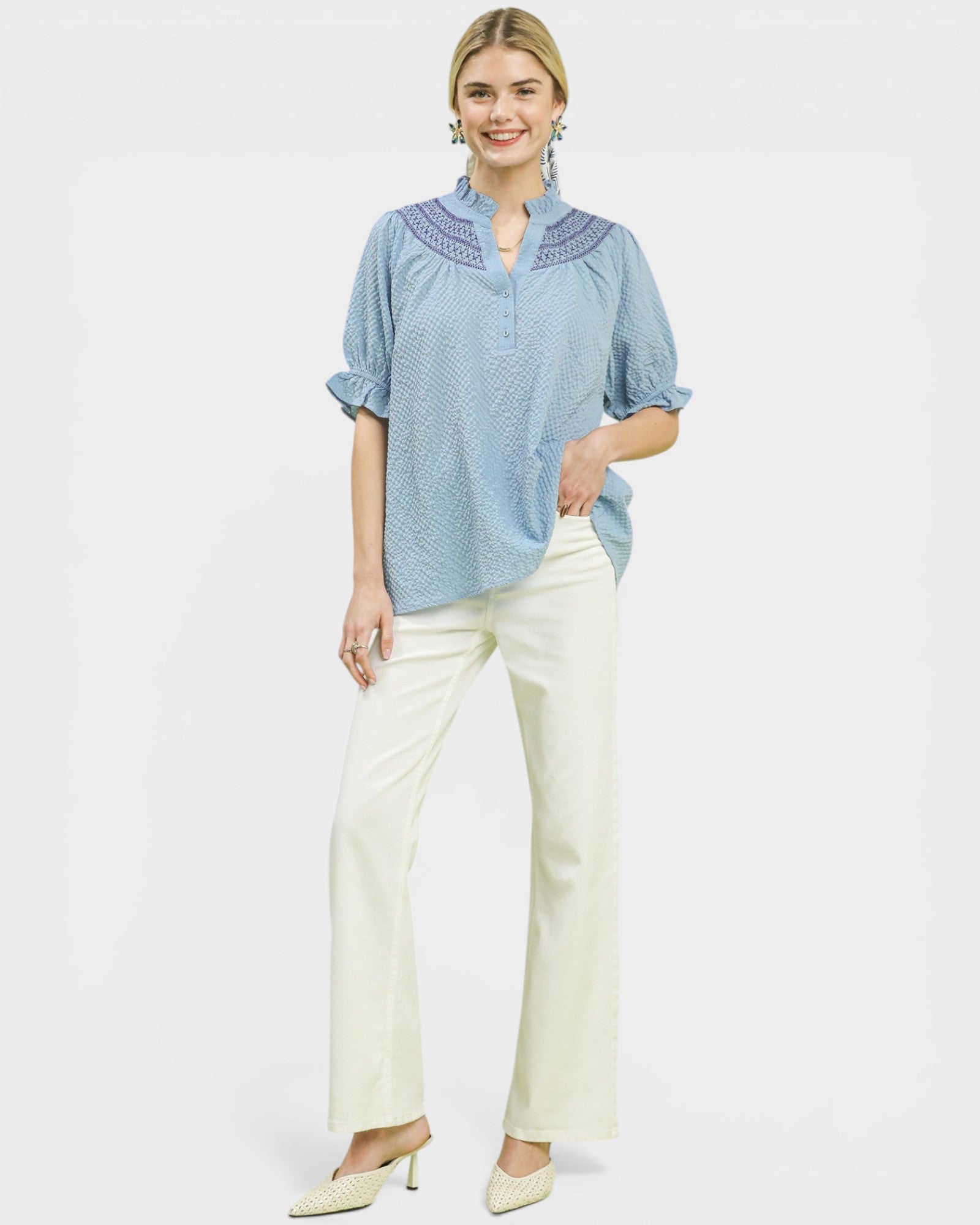 Woman wearing a blue patterned blouse and white pants on a white background