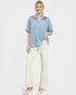 Woman wearing a blue patterned blouse and white pants on a white background