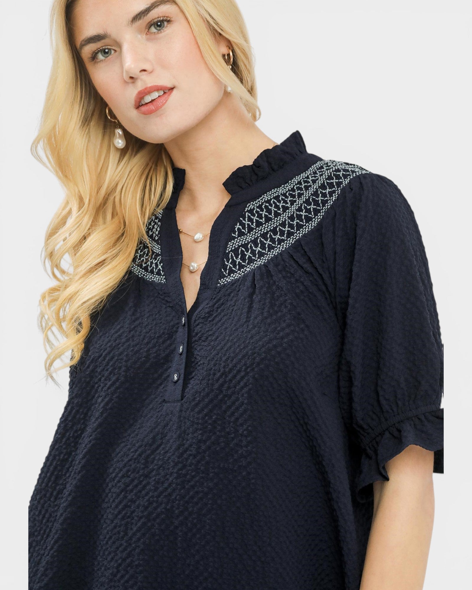 Woman wearing a navy blue dress with intricate white embroidery on a light gray background