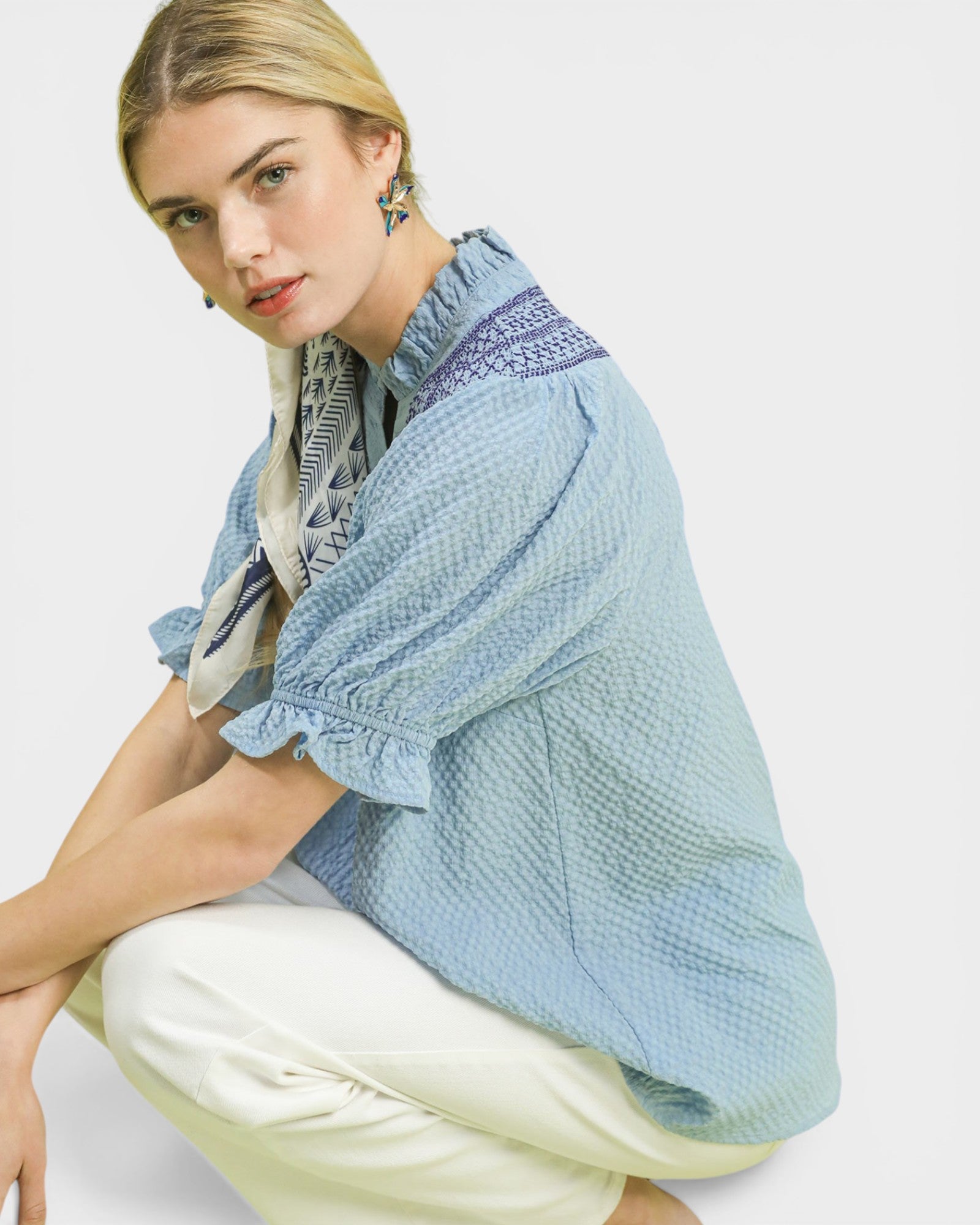 Woman wearing a light blue textured shirt with a patterned scarf on a white background