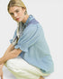 Woman wearing a light blue textured shirt with a patterned scarf on a white background