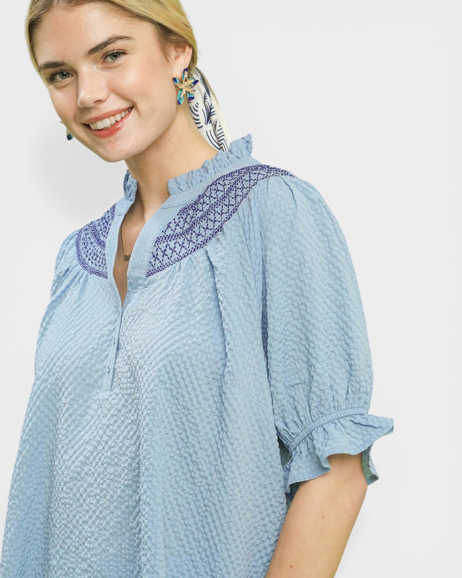 Woman wearing a light blue blouse with embroidered details on a white background