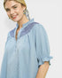 Woman wearing a light blue blouse with embroidered details on a white background