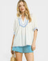 Woman wearing a white blouse with blue accents and blue shorts on a white background