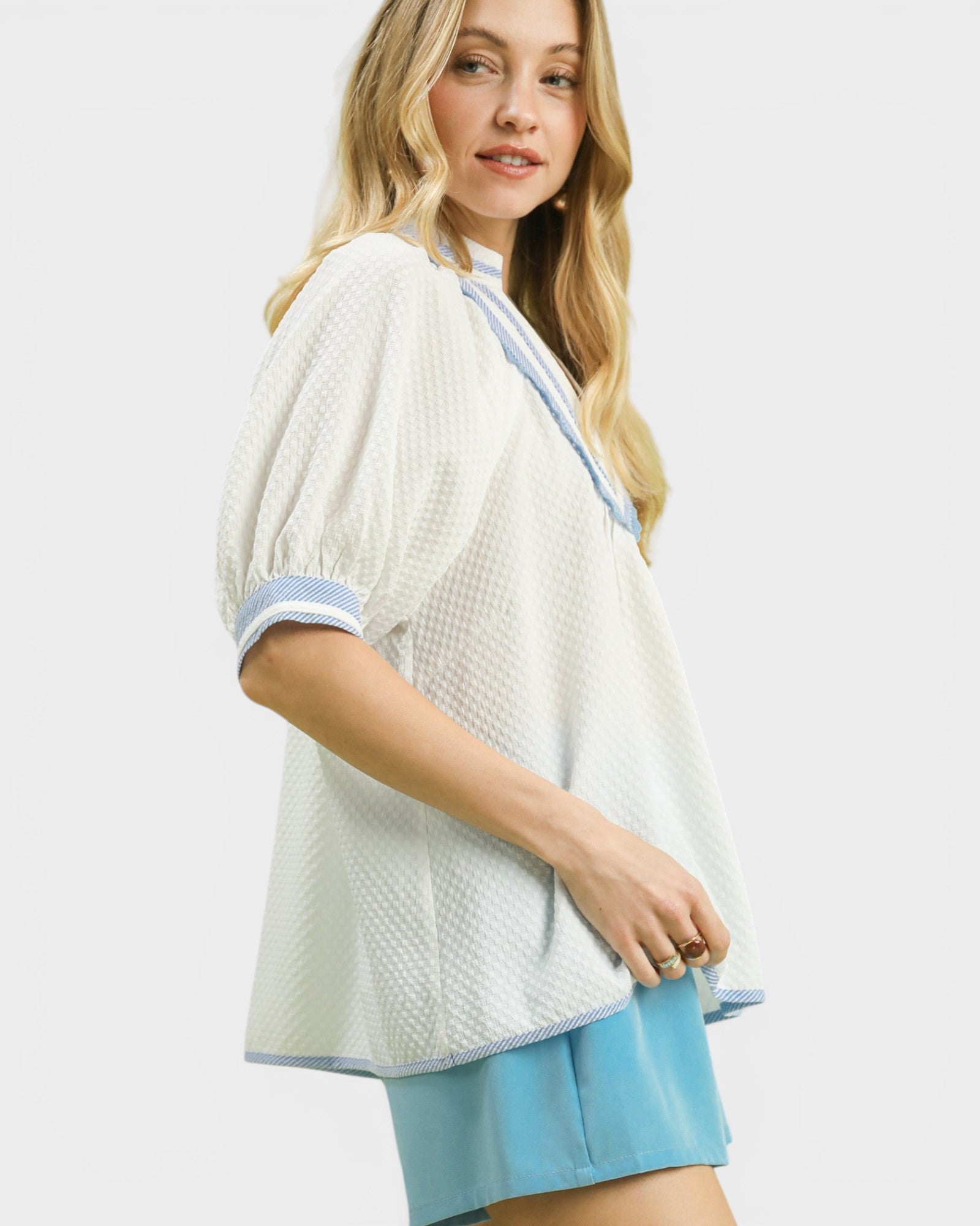 Woman wearing a white textured top with blue trim on a white background
