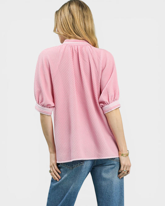 Person wearing a pink textured top and blue jeans on a white background