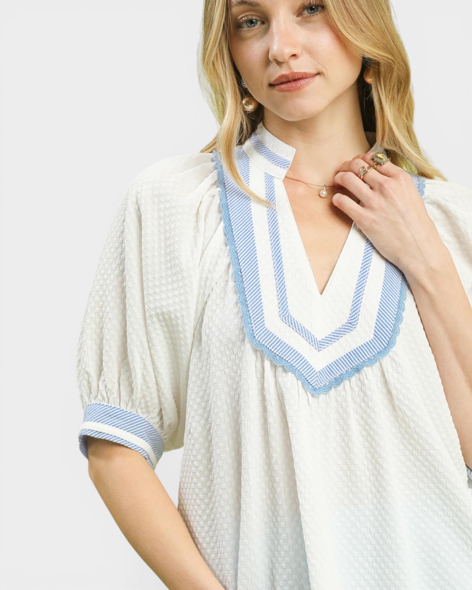 Woman wearing a white dress with blue trim on a plain background