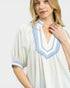 Woman wearing a white dress with blue trim on a plain background