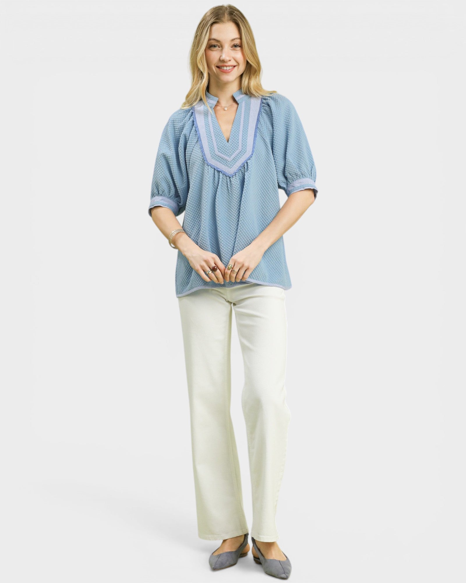 Woman wearing a blue blouse and white pants on a light gray background