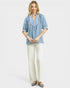 Woman wearing a blue blouse and white pants on a light gray background