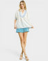 Woman wearing a white blouse with blue trim and light blue shorts on a white background
