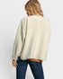 Person wearing a beige sweater with a subtle pattern on a plain background
