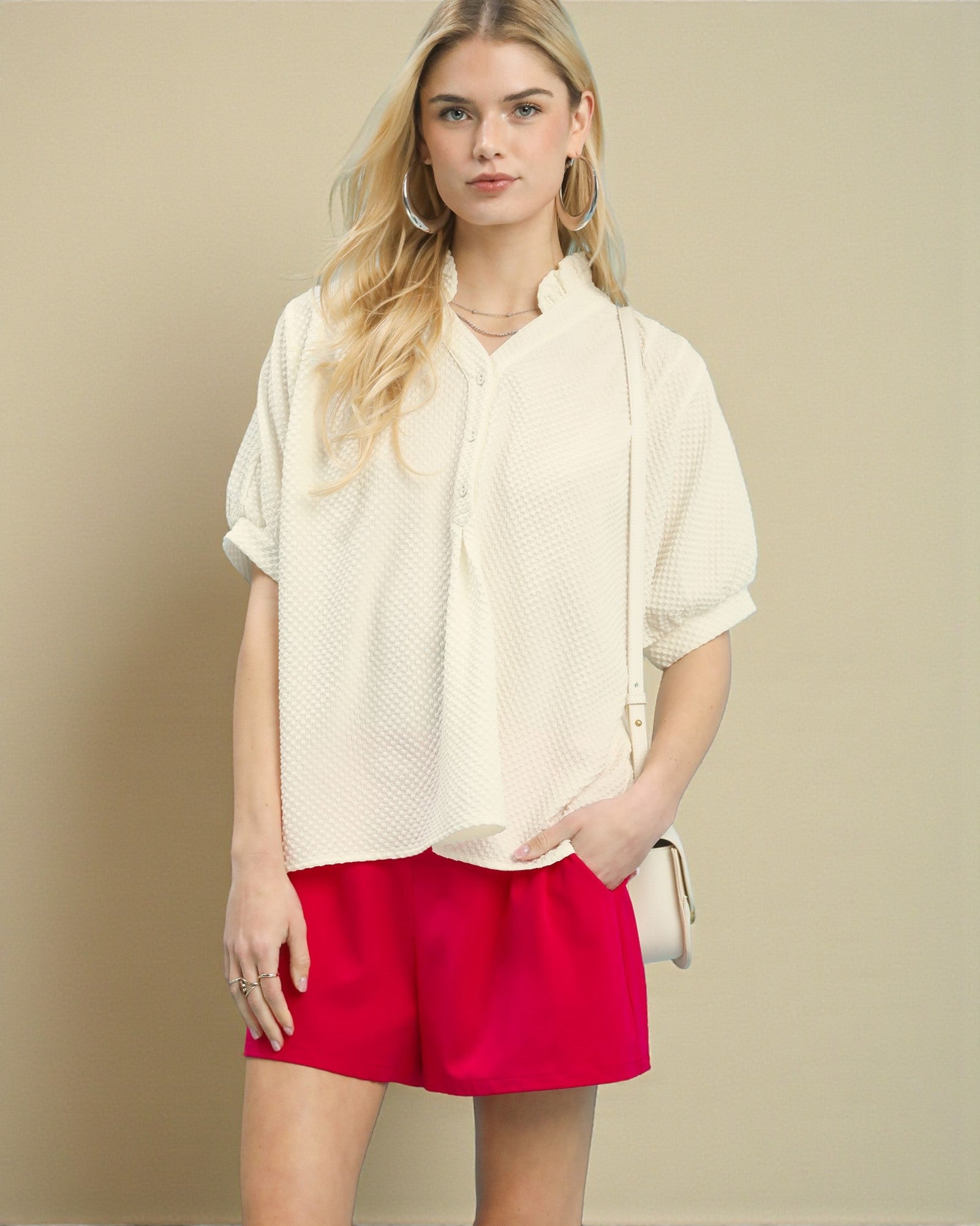 Woman wearing a cream blouse and red shorts against a beige background