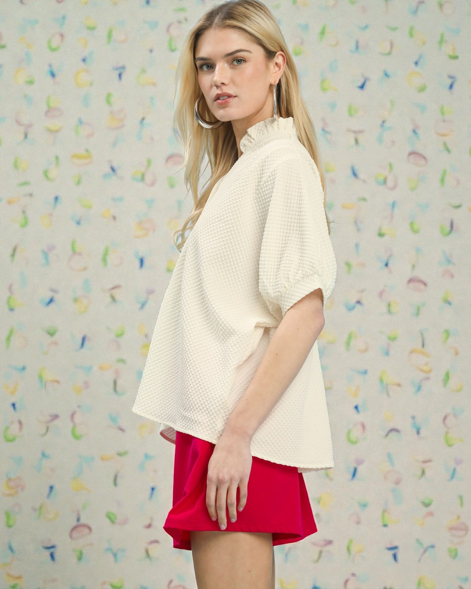 Woman wearing a white top and red shorts against a colorful patterned background