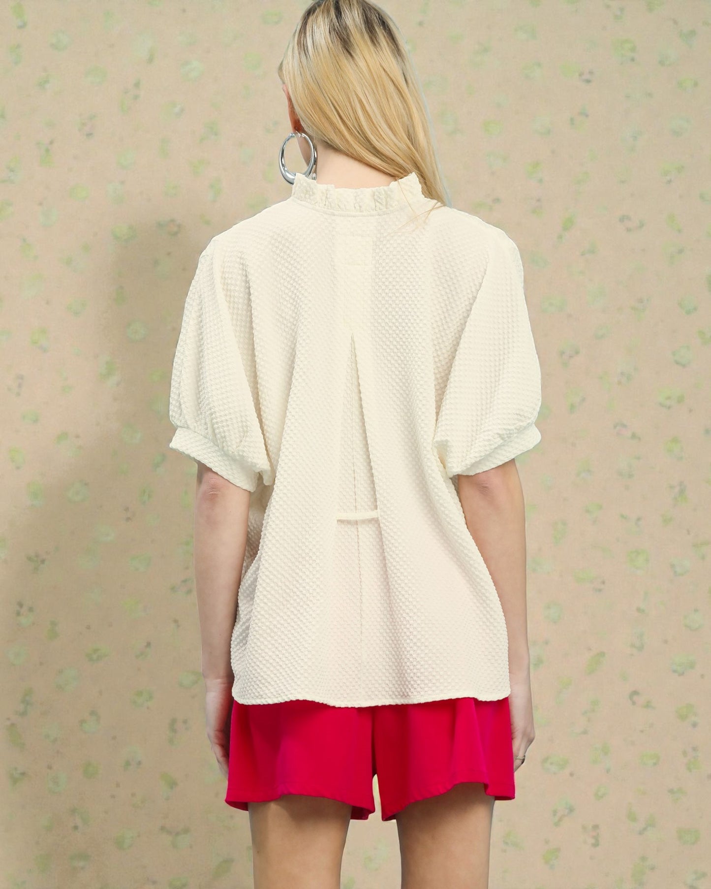 Person wearing a cream cardigan over a red skirt on a patterned beige background