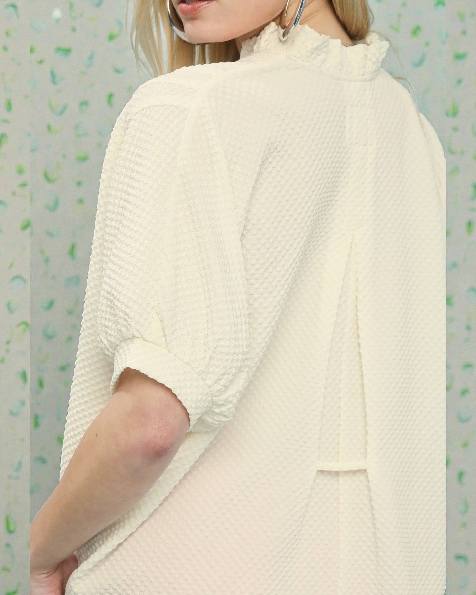 Person wearing a cream-colored textured sweater against a patterned background