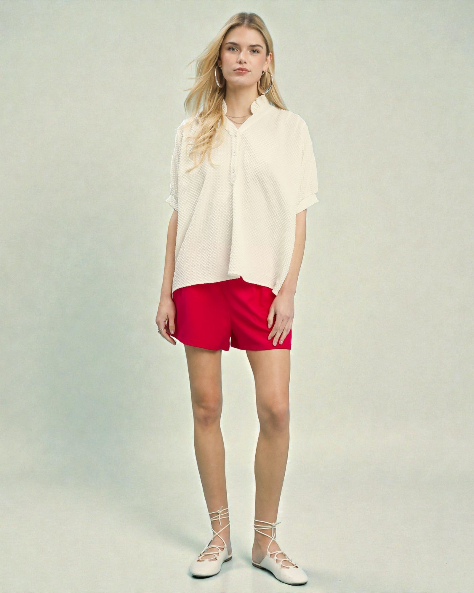 Woman wearing a white blouse and red shorts on a plain background
