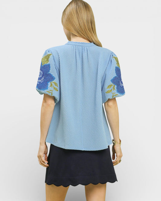 Woman wearing a light blue top with floral sleeves on a white background