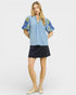 Woman wearing a light blue top with floral patterns and a black skirt on a white background