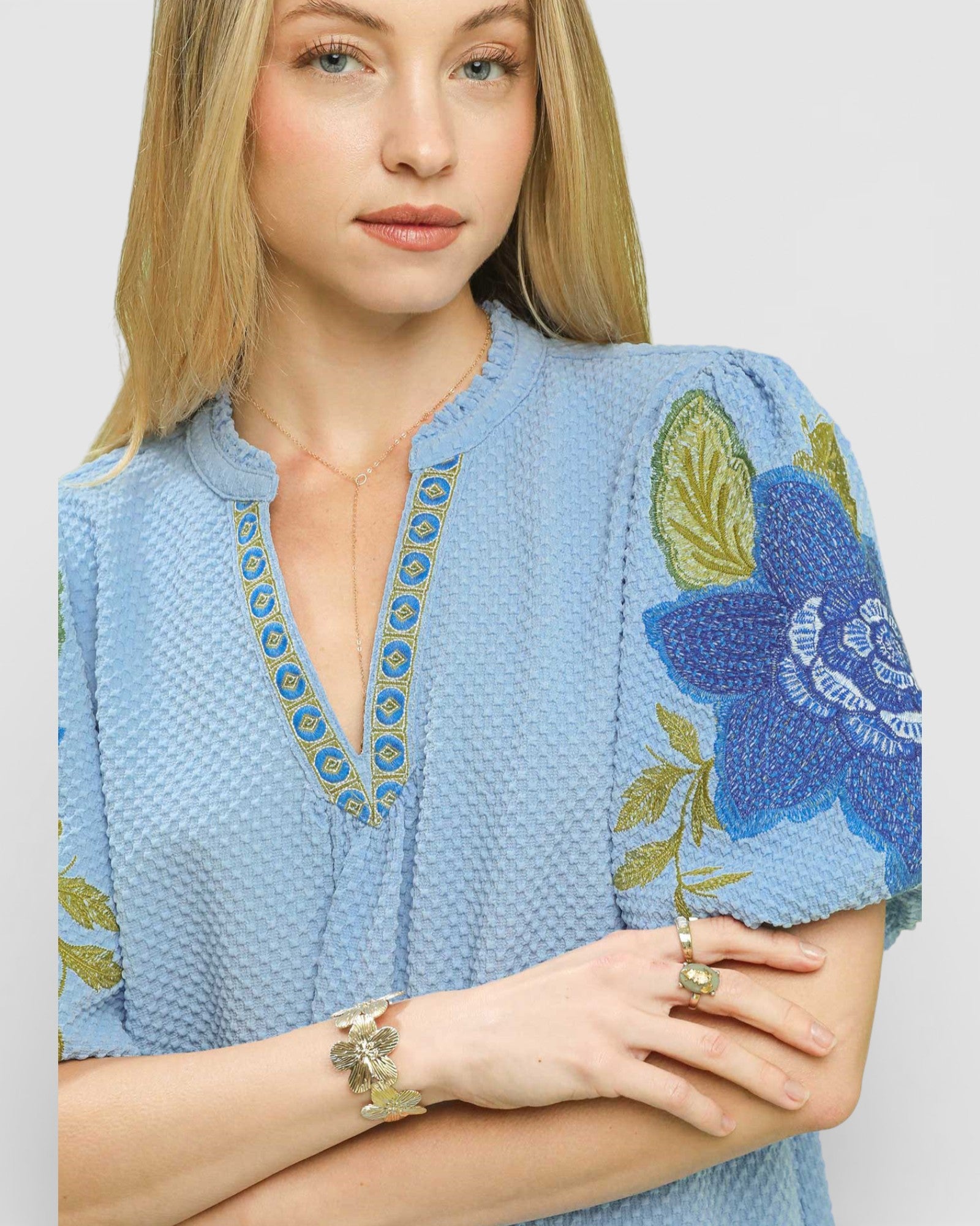 Woman wearing a blue embroidered top with floral designs on a plain background