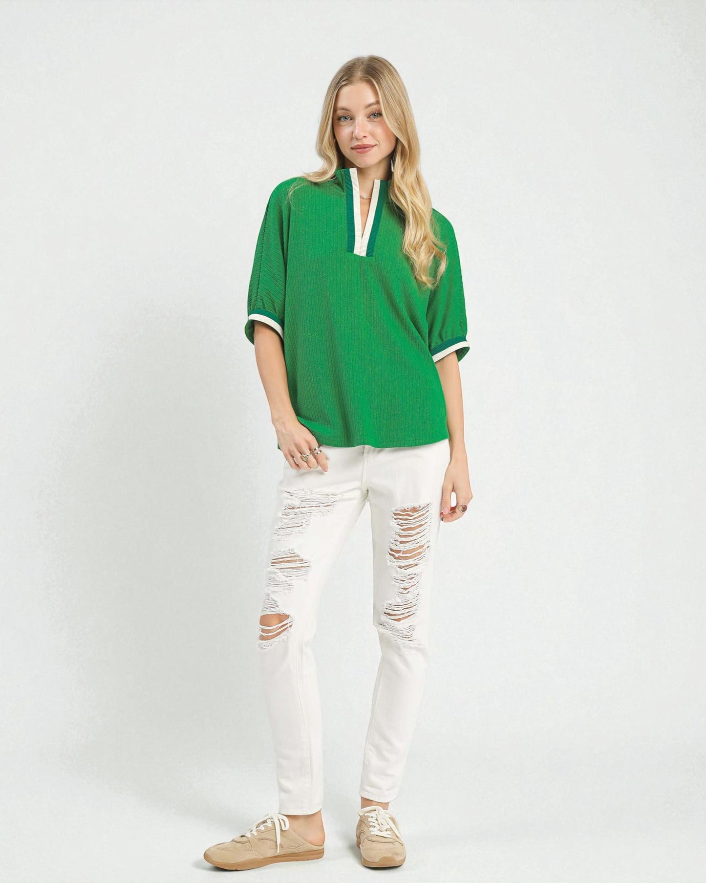 Woman wearing a green top and white distressed jeans on a white background