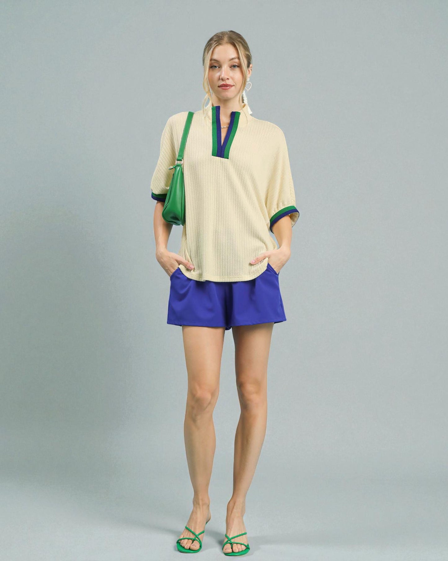 Woman wearing a beige top and blue shorts with a green bag on a gray background