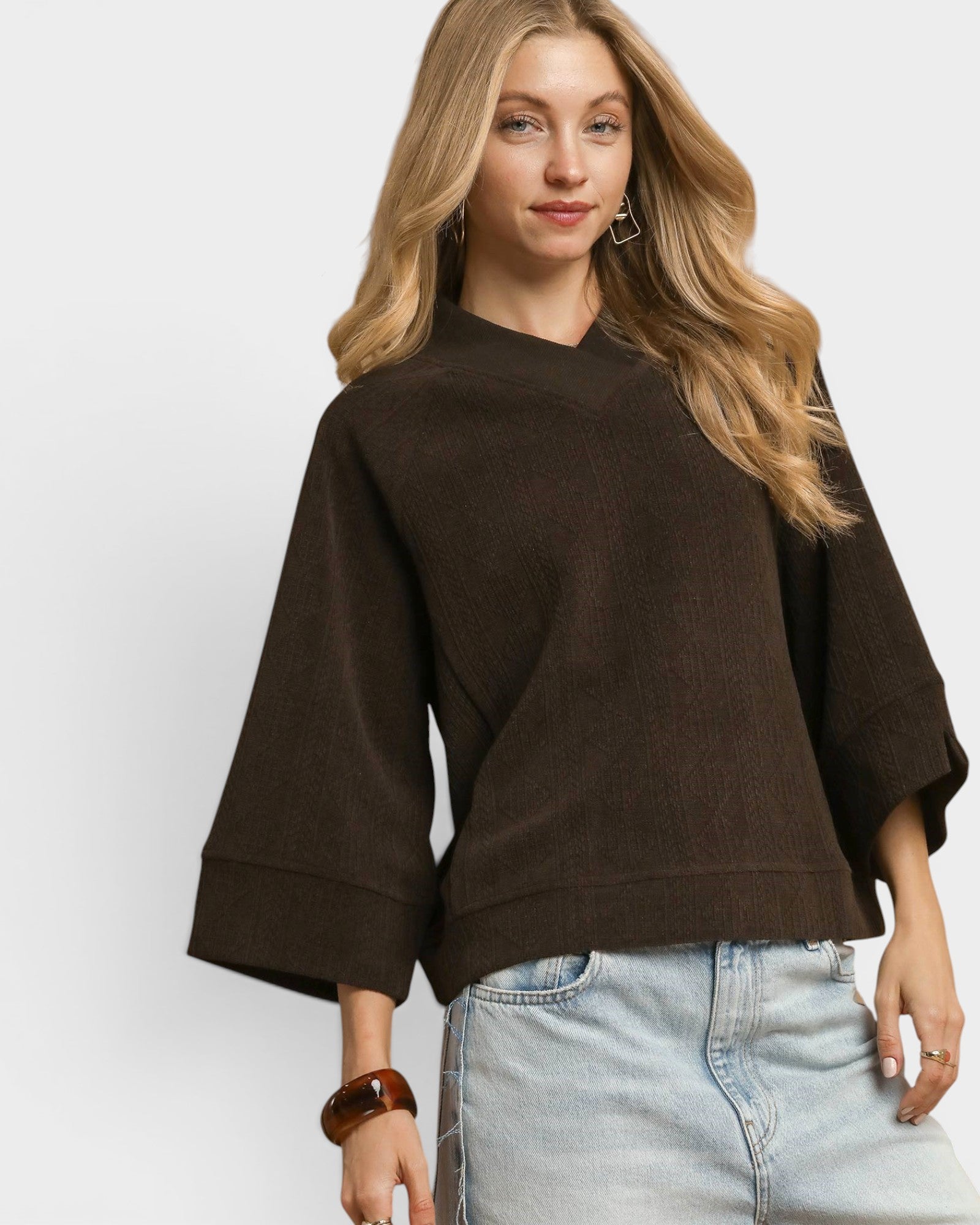 Woman wearing a brown sweater and light blue jeans on a white background