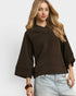 Woman wearing a brown sweater and light blue jeans on a white background