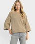 Woman wearing a beige sweater and gray pants on a white background