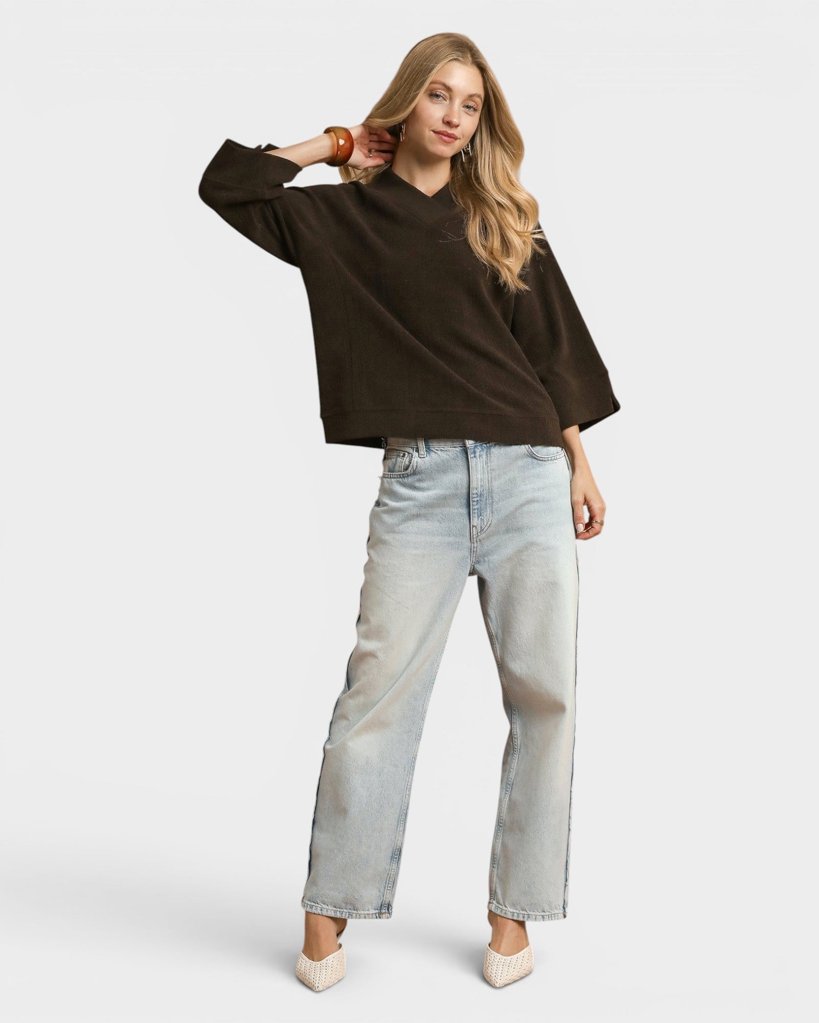Woman wearing a brown sweater and light blue jeans on a white background