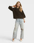 Woman wearing a brown sweater and light blue jeans on a white background