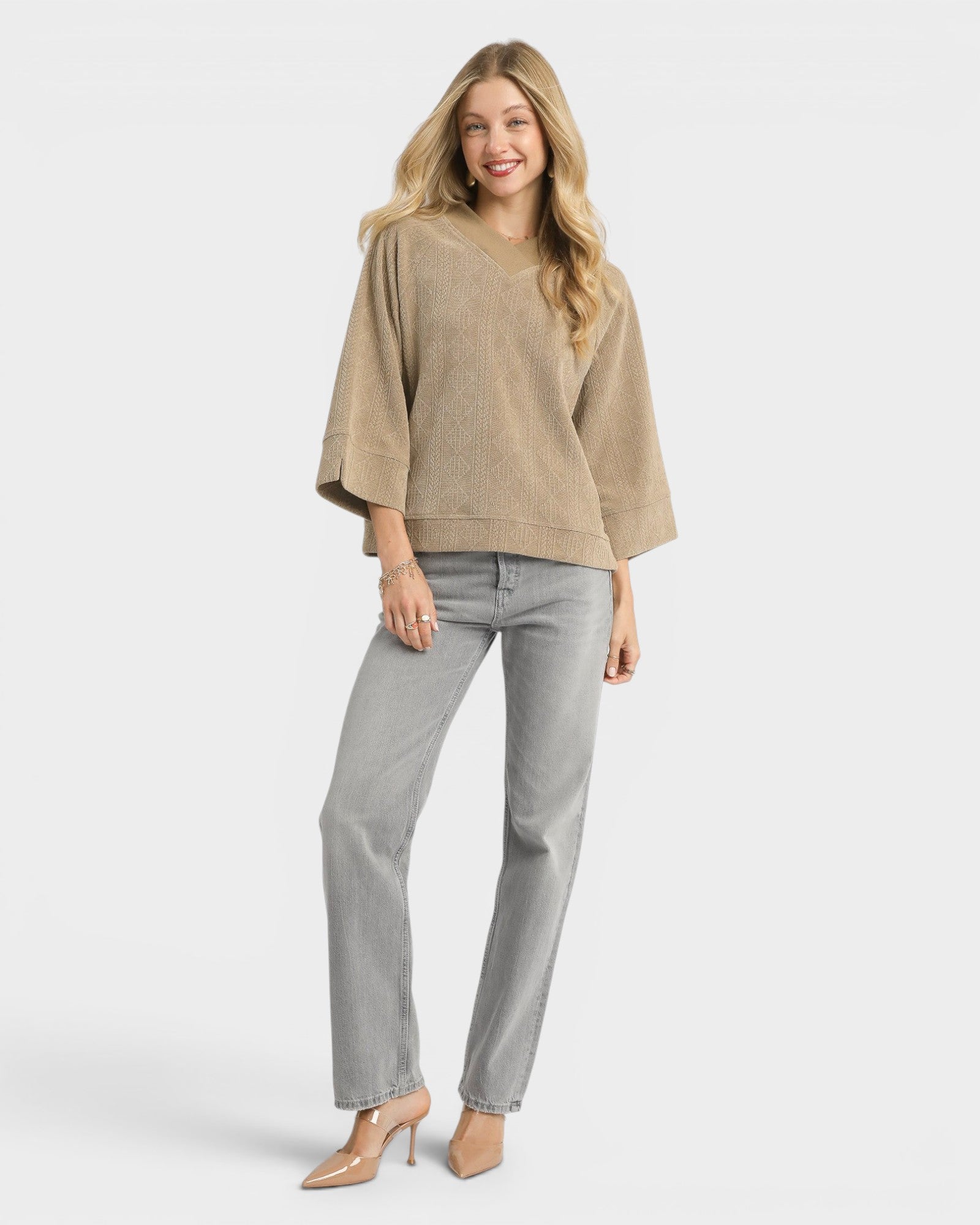 Woman wearing a beige sweater and gray jeans on a white background