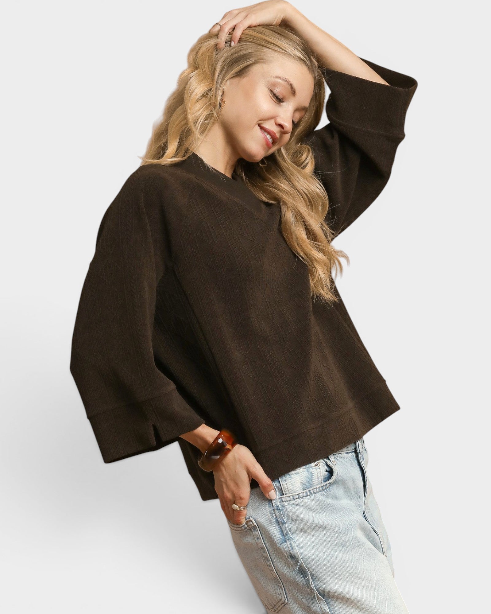 Woman wearing a brown sweater and light blue jeans on a white background