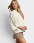 Woman wearing a cream sweater and beige shorts on a light gray background